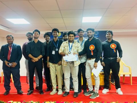 Jaikiran holding certificate of excellence with team and university faculty dignitaries on auditorium stage